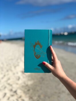 Couverture d’un Moleskine illustrée par Yollema pour le magazine URBANIA, photographiée sur un fond de plage.