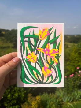 Carte postale illustrée de tulipes en risographie par Yollema, tenue par une main sur fond de prairie