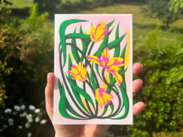 Carte postale illustrée de tulipes au en risographie par Yollema, tenue par une main sur fond de prairie 