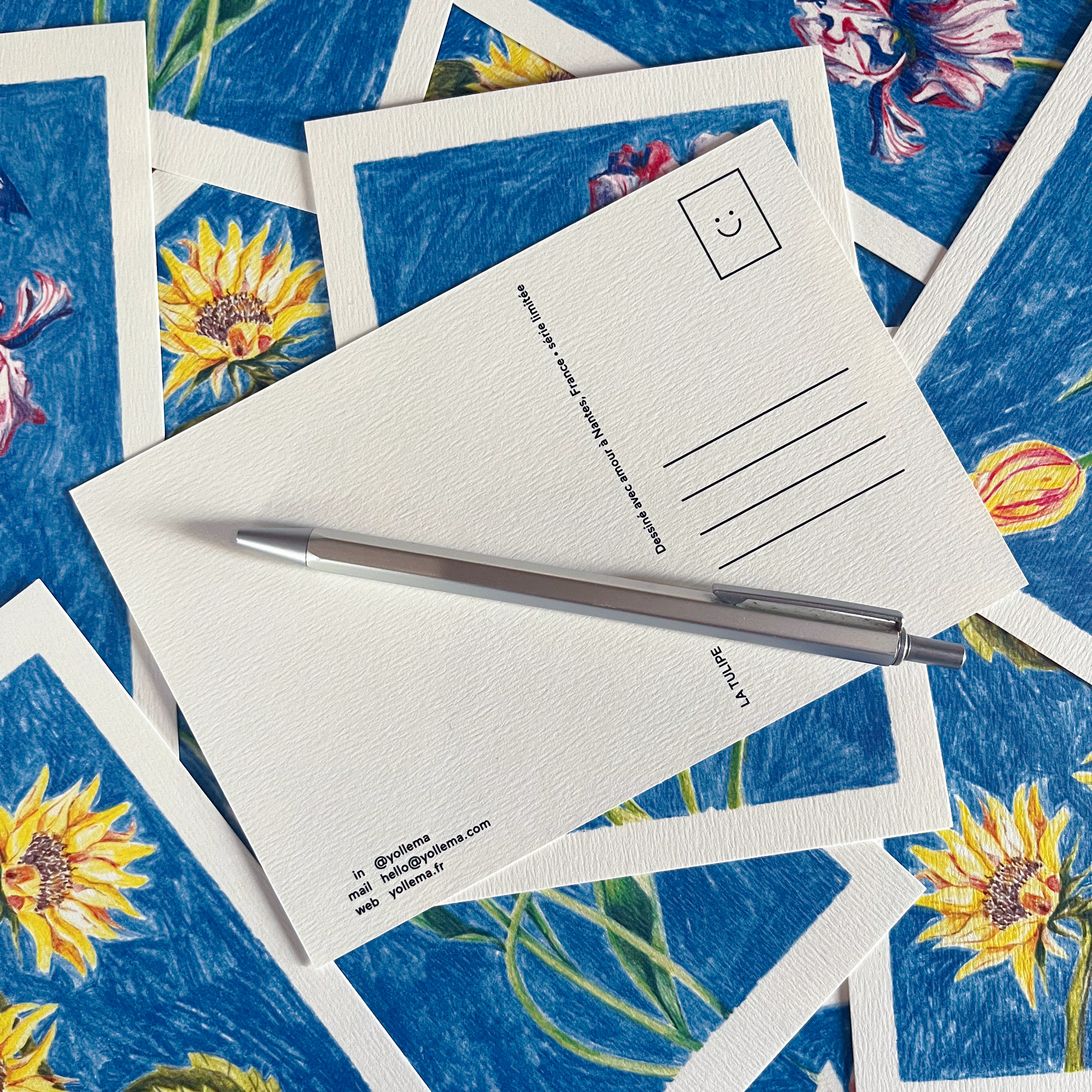 Verso d'une carte postale fleurie par Yollema posée sur une pile de cartes postale