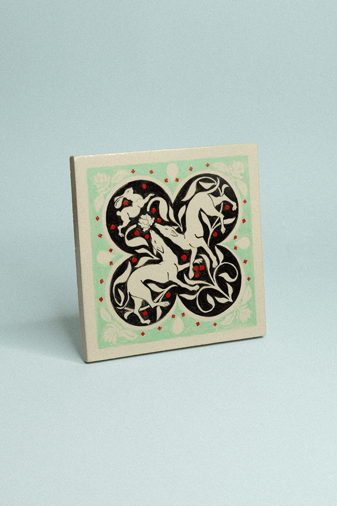 Carreau en grès peint à la main en ton crème, vert pâle et noir avec motif floral symétrique représentant deux lévriers et un lapin.