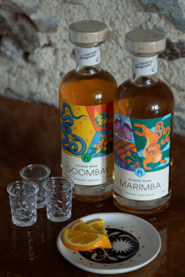 Deux bouteilles de rhum avec des étiquettes illustrées, trois petits verres et des tranches d'orange 