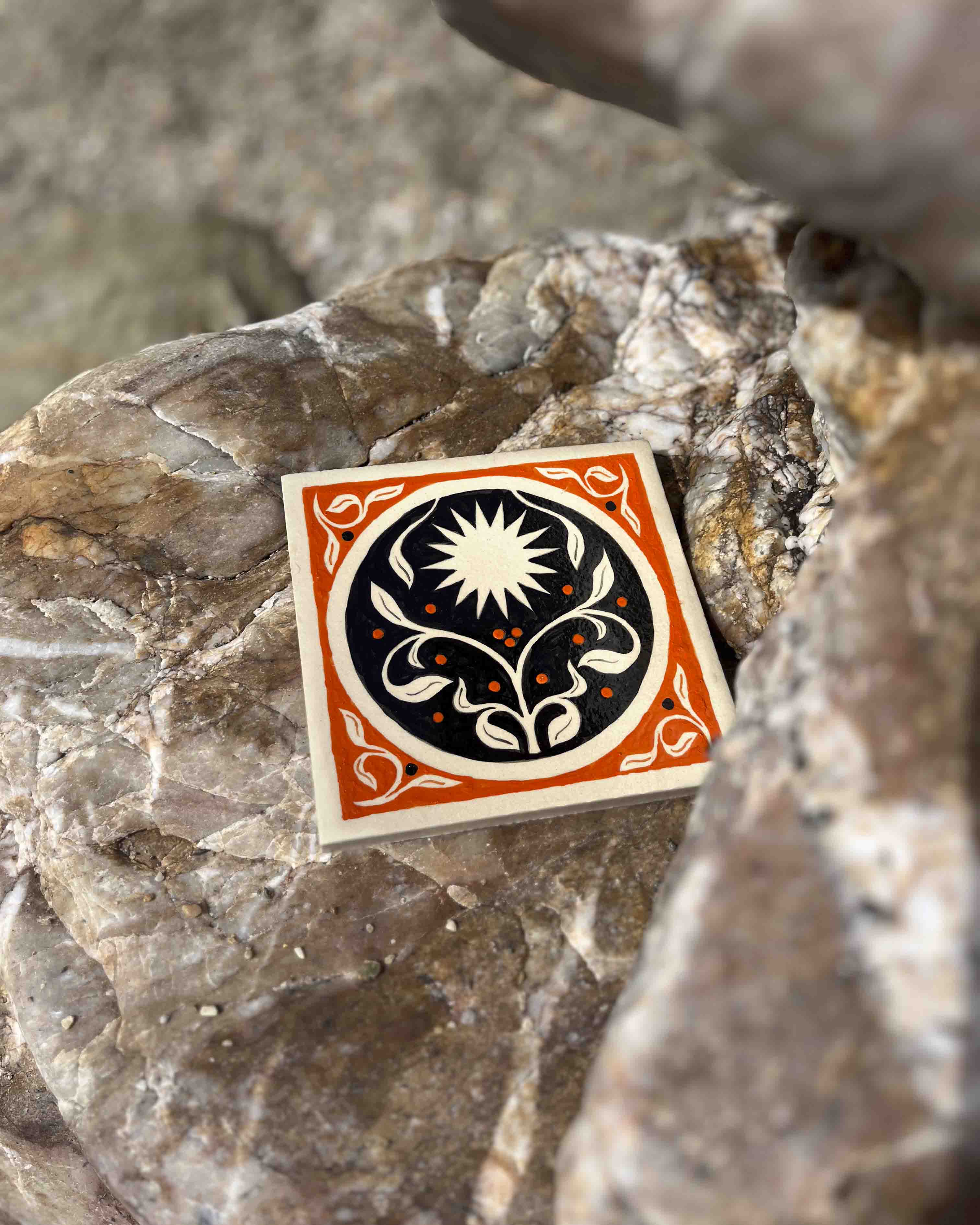 Carreaux de grès orange et noir illustré par Yollema représentant un soleil et un motif floral sur un rocher
