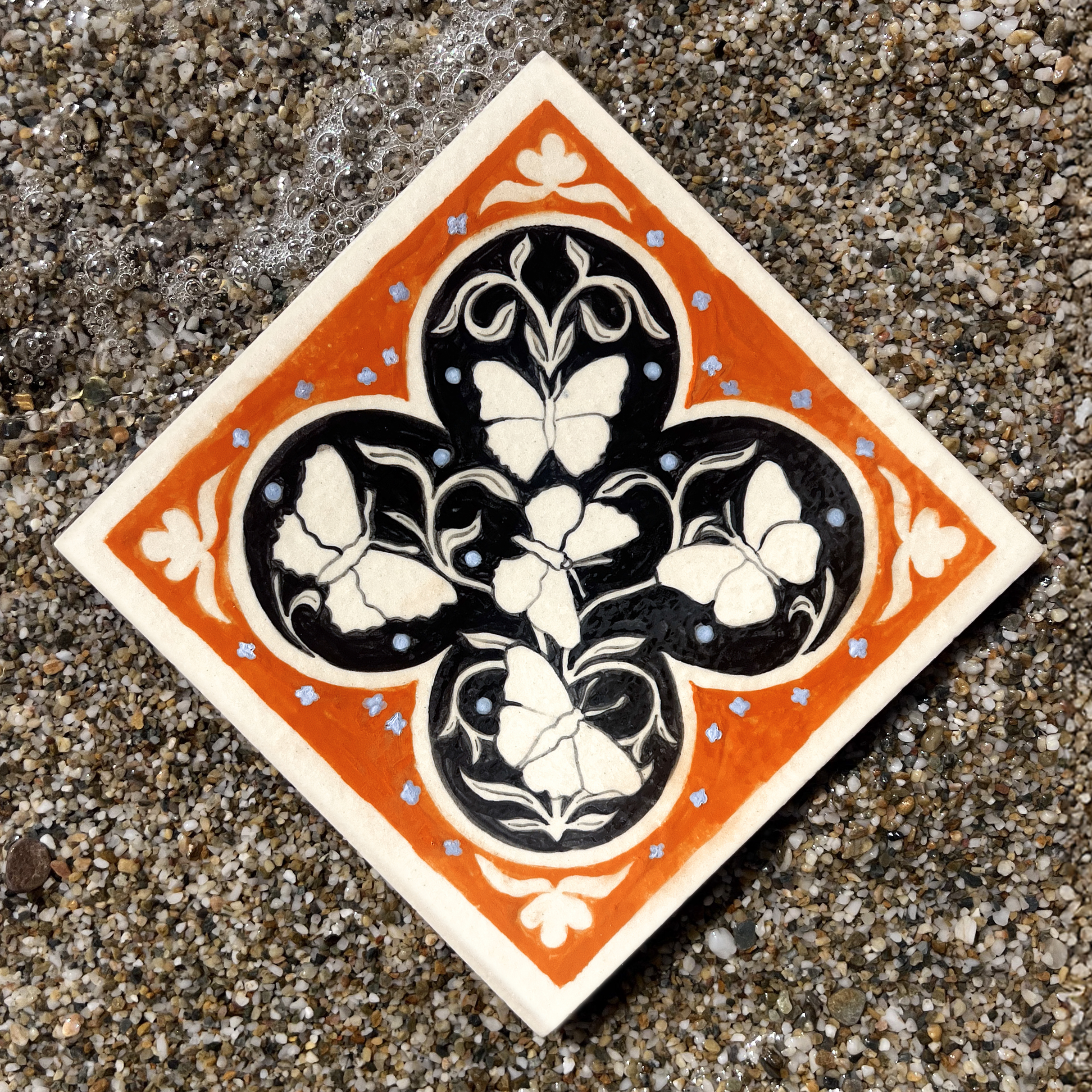 Carreau en grès illustré avec cinq papillons et un motif végétal orange et noir par Yollema