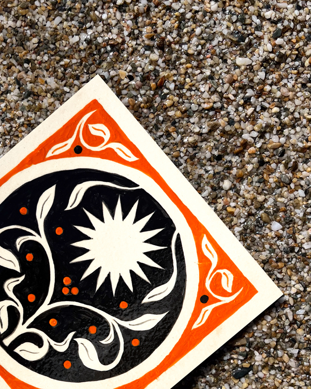 Détail d'un carreaux de grès en bas à gauche orange et noir peint à la main avec un soleil par Yollema