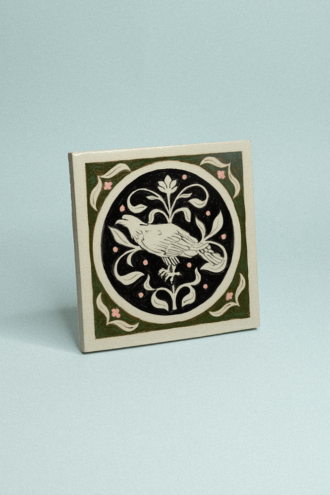 Carreau de grès décoratif, peint à la main, vert foncé et noir représentant un aigle et un motif floral en fond.
