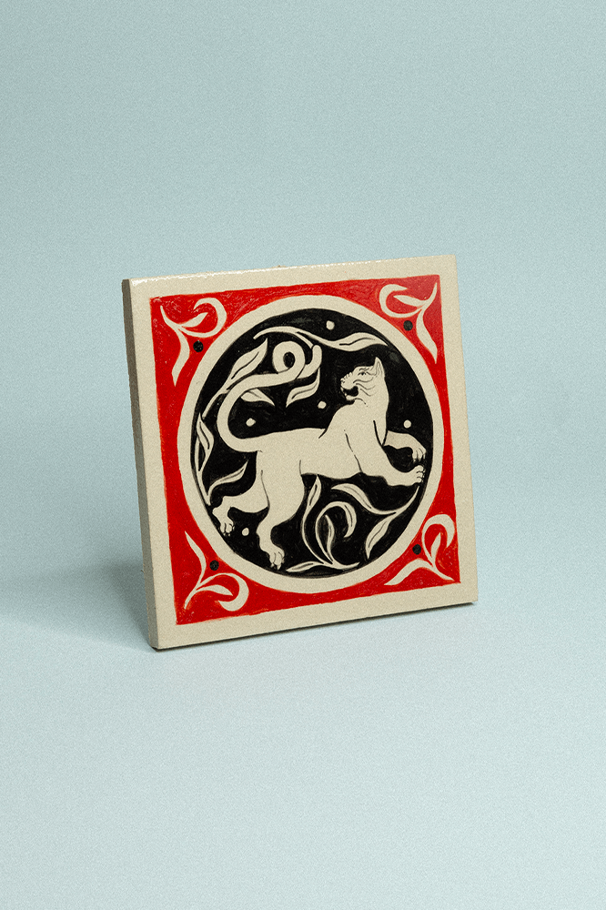 Carreau de grès décoratif, peint à la main, rouge et noir représentant un chat et un motif floral en fond.