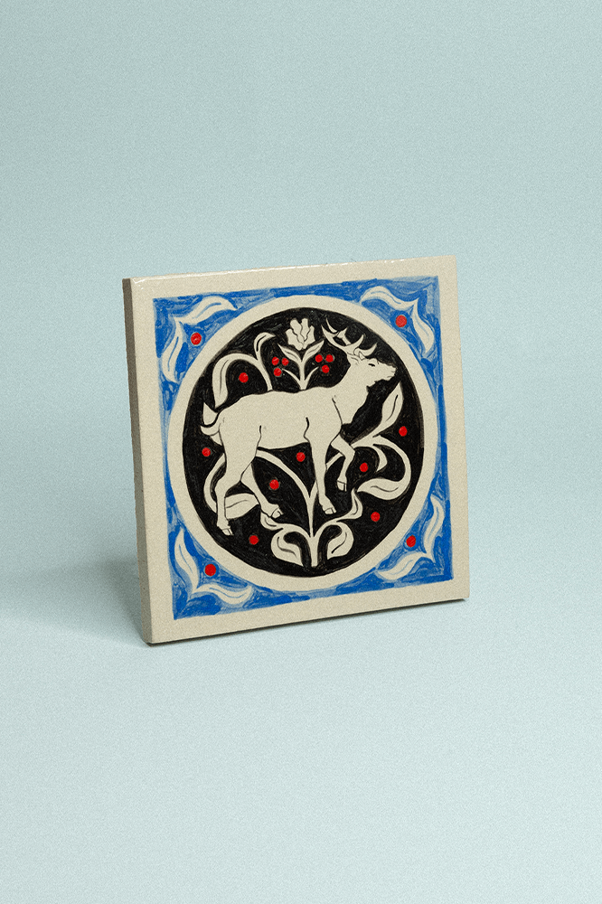 Carreau de grès décoratif, peint à la main, bleu et noir représentant un cerf et un motif floral en fond.
