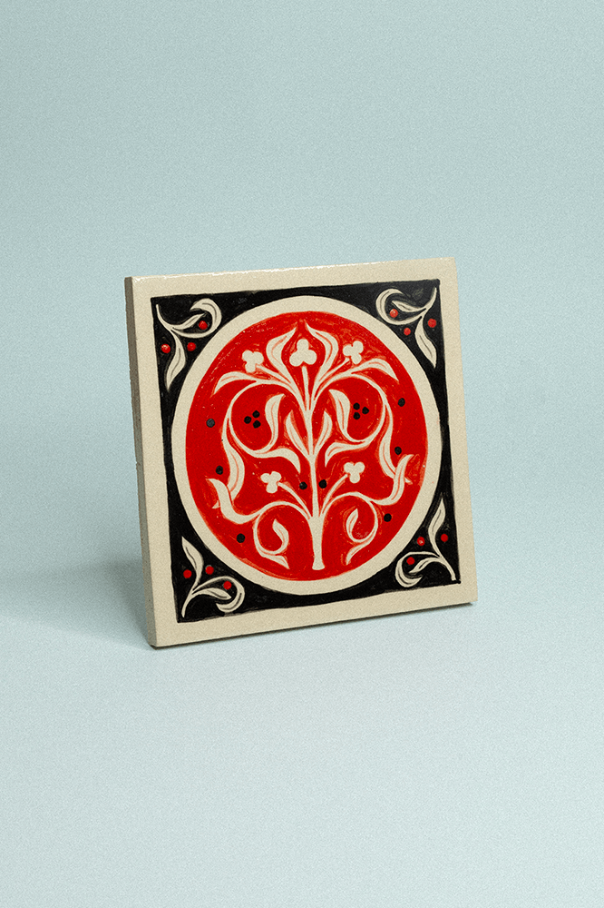 Carreau de grès décoratif, peint à la main, rouge et noir avec un motif floral symétrique.