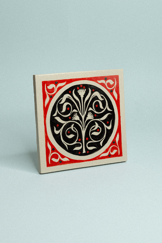 Carreau de grès décoratif, peint à la main, rouge et noir avec un motif floral symétrique.