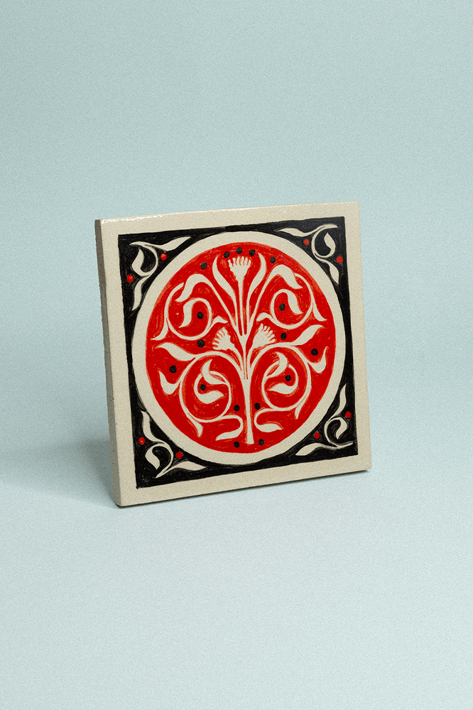 Carreau de grès décoratif, peint à la main, rouge et noir avec un motif floral symétrique.