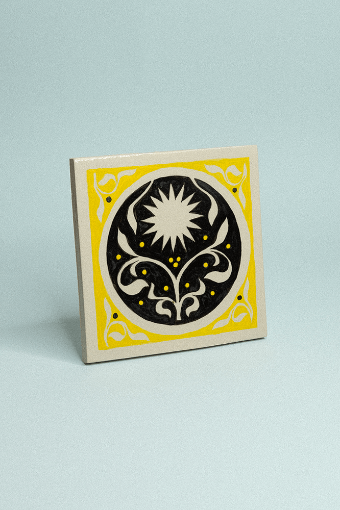 Carreau de grès décoratif, peint à la main, jaune et noir avec un soleil et un motif floral symétrique.
