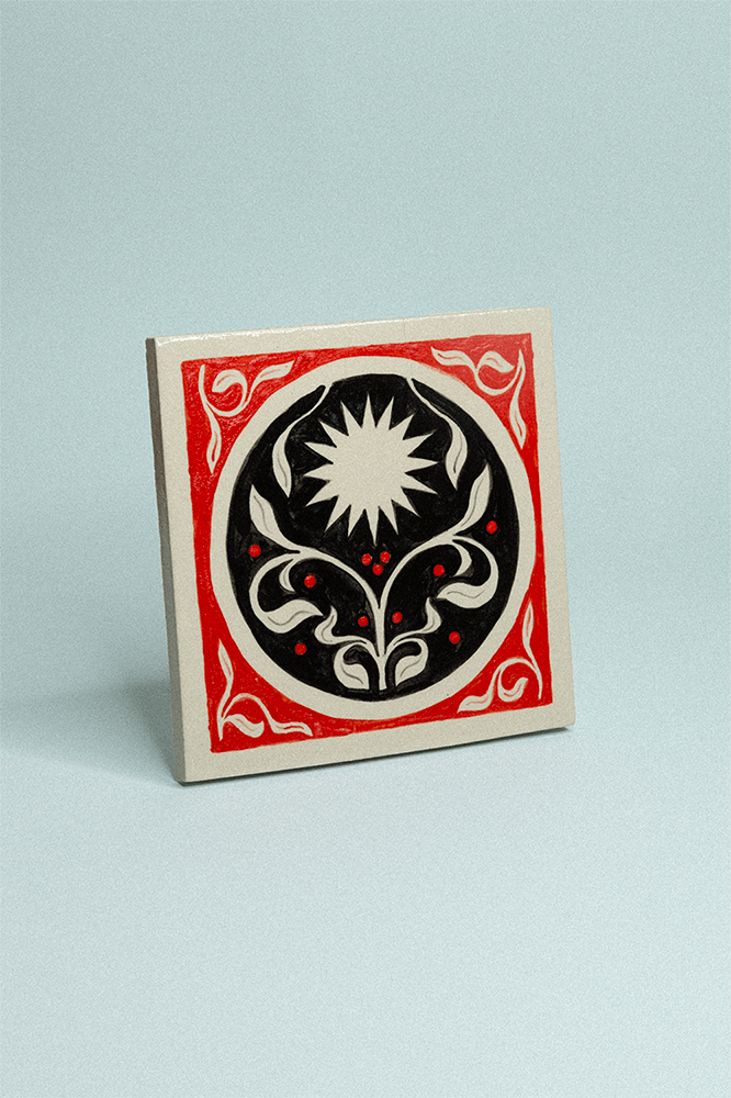 Carreau de grès décoratif, peint à la main, rouge et noir avec un soleil et un motif floral symétrique.