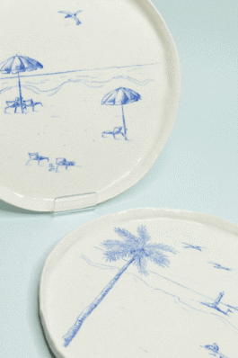 Zoom sur deux assiettes en porcelaine blanche, illustration bleu cobalt représentant plages et parasols. 